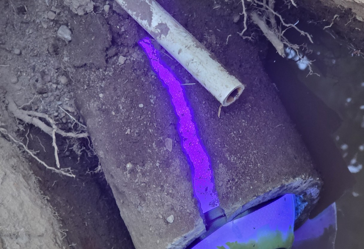 UV dye trace marking a crack in an old concrete side sewer line in an open excavation